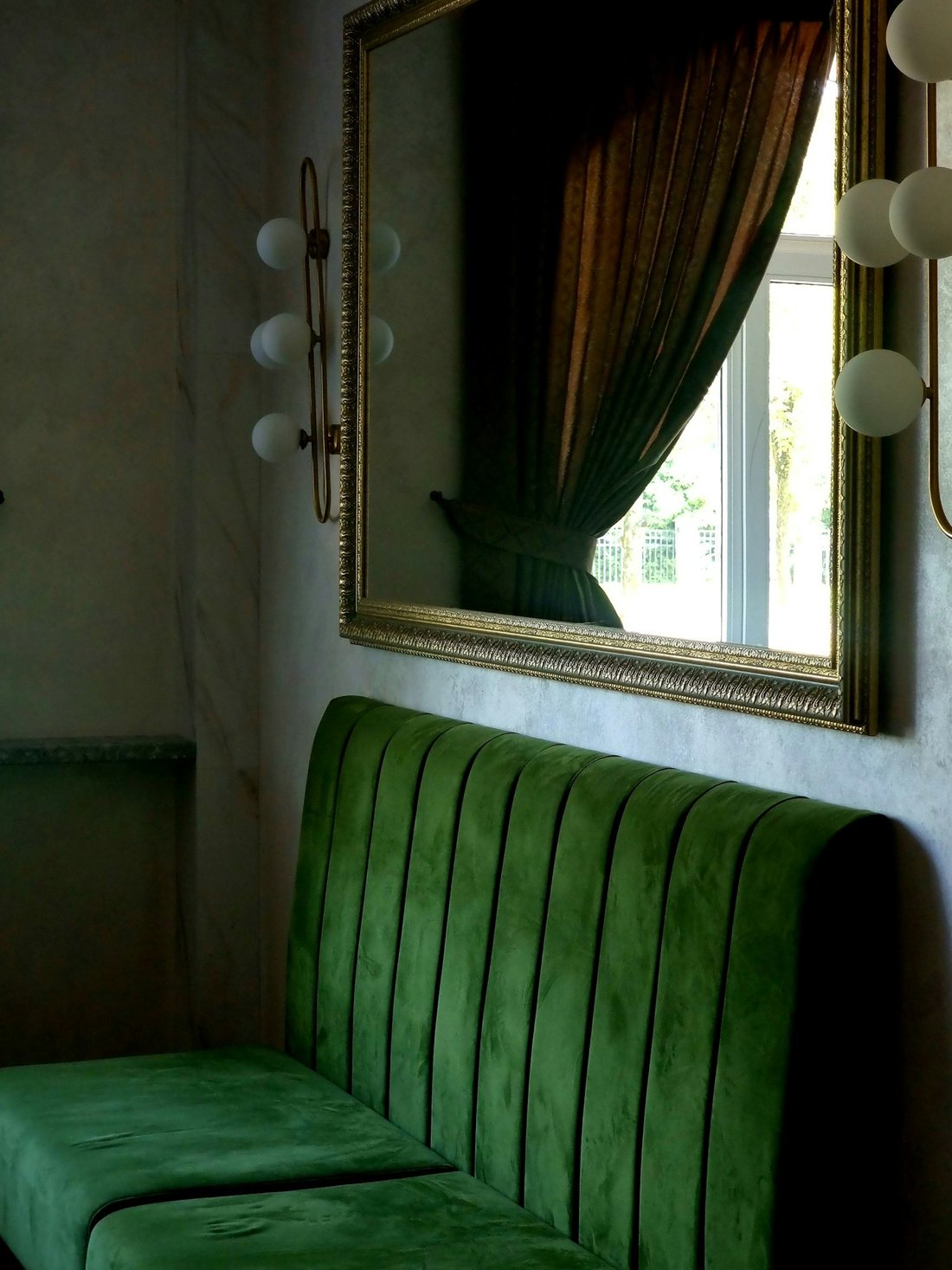 Dybgrøn velour-sofa under et guldindrammet spejl